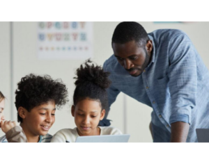 Diverse group of children with male teacher using laptop together in modern school classroom